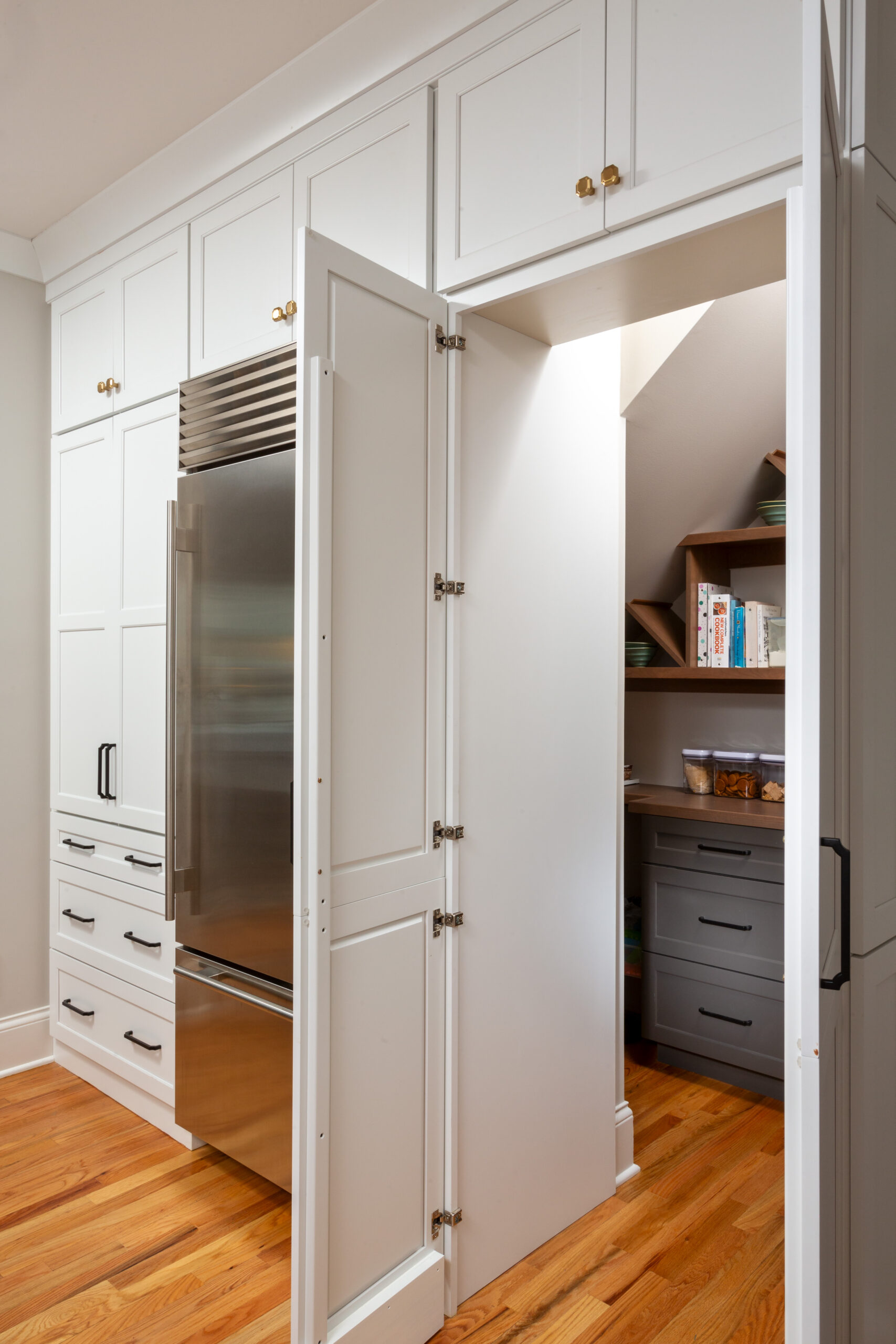Hidden walk-in pantry concealed behind double cabinet doors in white shaker kitchen cabinetry.